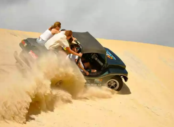 na imagem, vemos um buggy passando nas dunas de uma praia de Natal. na imagem, o veículo está em alta velocidade, ilustrando o que seria uma passeio de buggy com emoção.