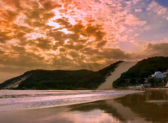 na imagem, vemos o Morro do Careca, paisagem famosa em Natal, com o céu em tons alaranjados. A foto foi feita durante o por do sol em Natal.